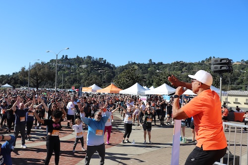 A group of run/walk participants being led in an exercise class by a man in an orange shirt and white hat