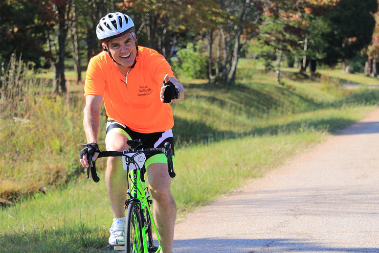 Male biker on country road smiling at camera with a thumbs up.