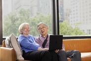 A seated couple smile while sharing a laptop.