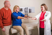 Male care partner alongside female patient undergoing Parkinson's test with her female physician.