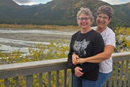 A couple pose in front of a mountain landscape. 