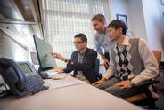 Three men in an office looking at a computer screen.