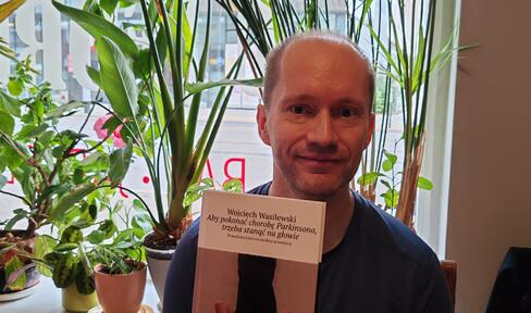 Wojciech Wasilewski smiling and holding a copy of his book in Polish.