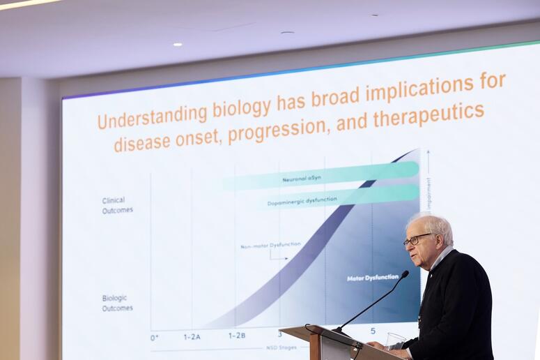 A man speaks at a podium with a graph in the background.