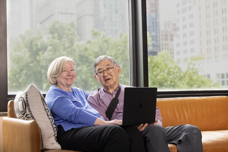A couple smile together seated on a couch.
