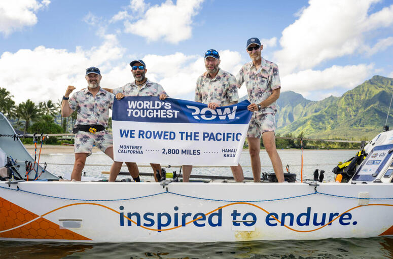 The four members of the World’s Toughest Row stand with a banner on their rowboat.