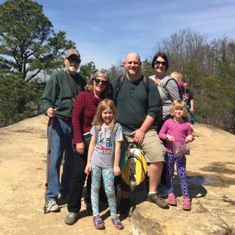 A family of seven stands together on a large rock.