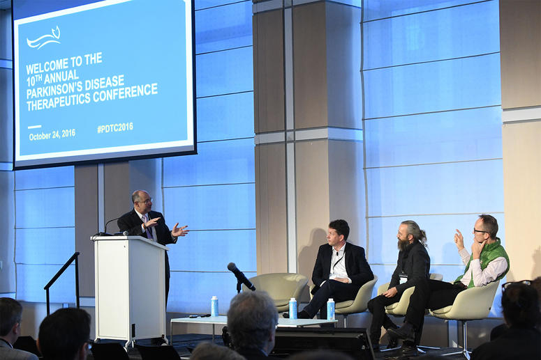 Speaker on stage with panelists at the Parkinson's Disease Therapeutics Conference.
