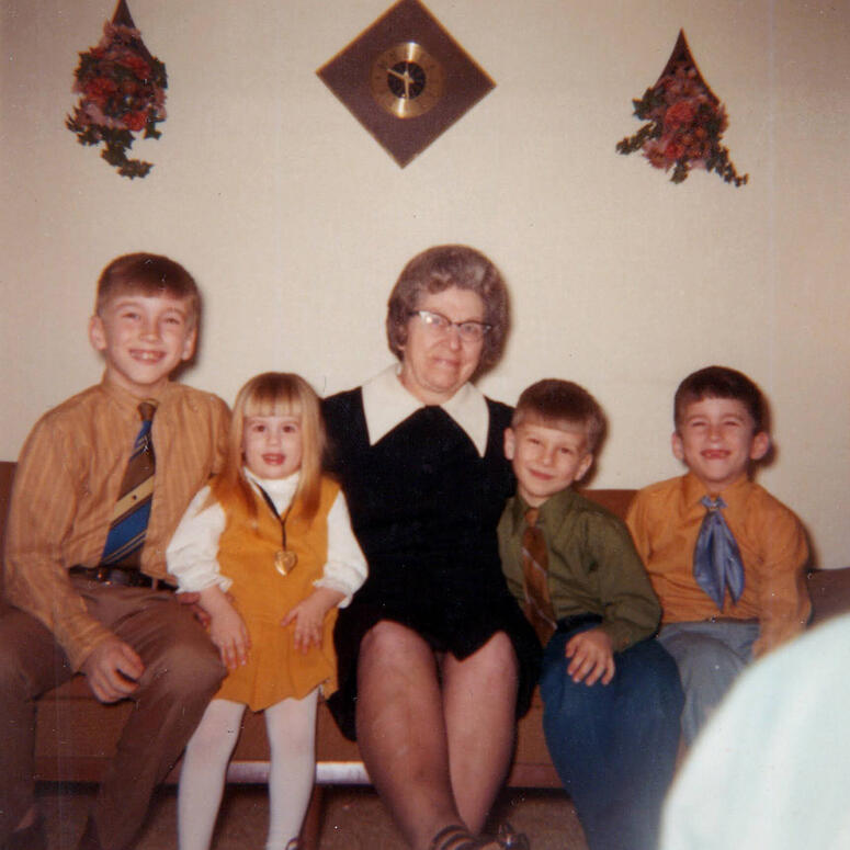 An old photograph of a grandmother sitting on a couch with four of her young grandchildren. 