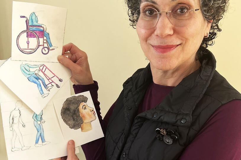 A woman holds up her illustrations.
