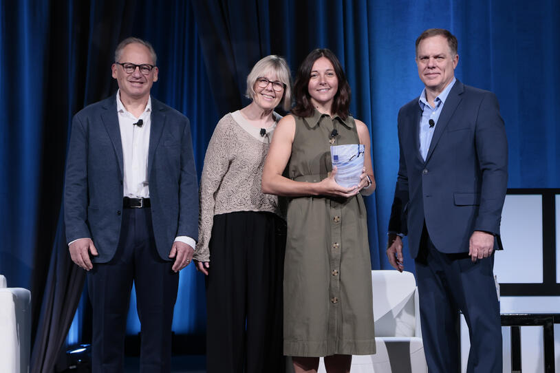 Four people looking at camera with one holding an award