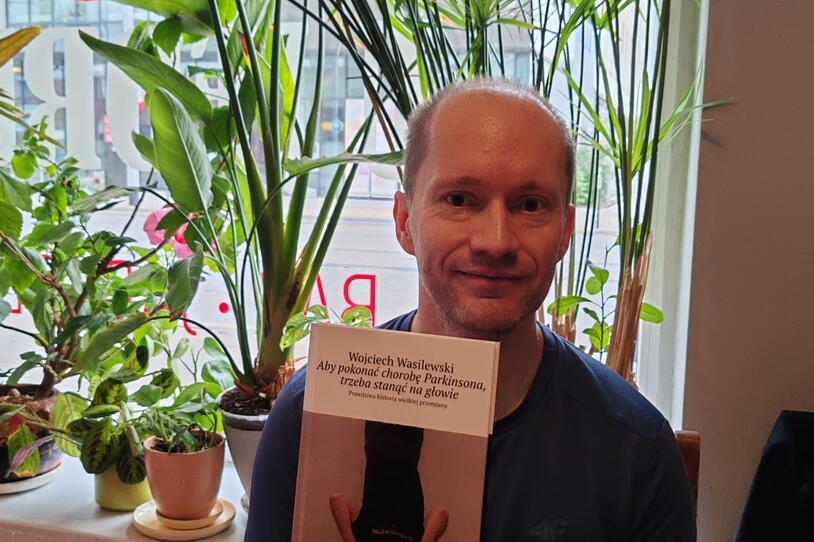 Wojciech Wasilewski smiling and holding a copy of his book in Polish.