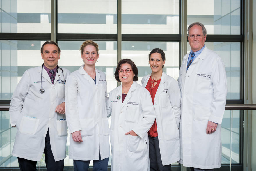 Three female and two male doctors all in white coats posing for camera.