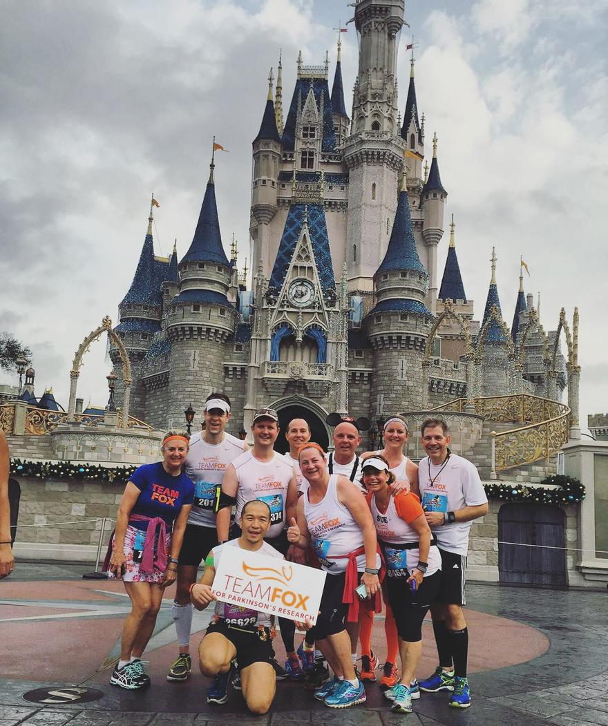 Group of Team Fox runners at the Walt Disney World Marathon holding a Team Fox sign in front of the Cinderella Castle.