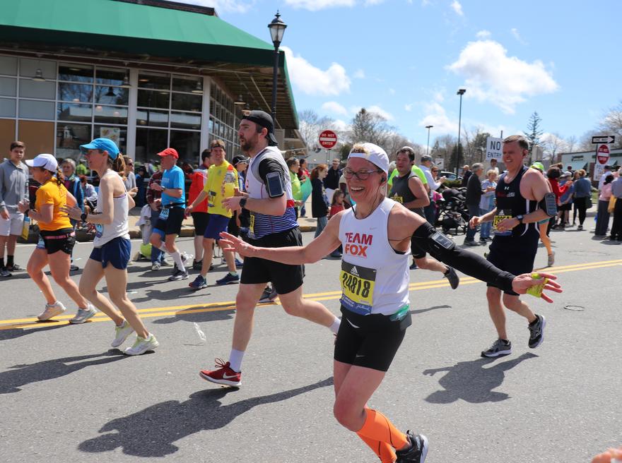 woman running in a Team Fox jersey with her arms open and smiling during the Boston Marathon
