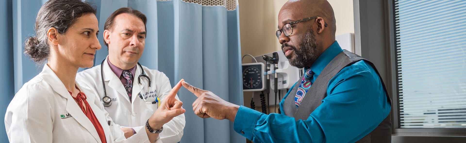 A patient in a doctor's office touching fingers with a physician while another physician observes the test.