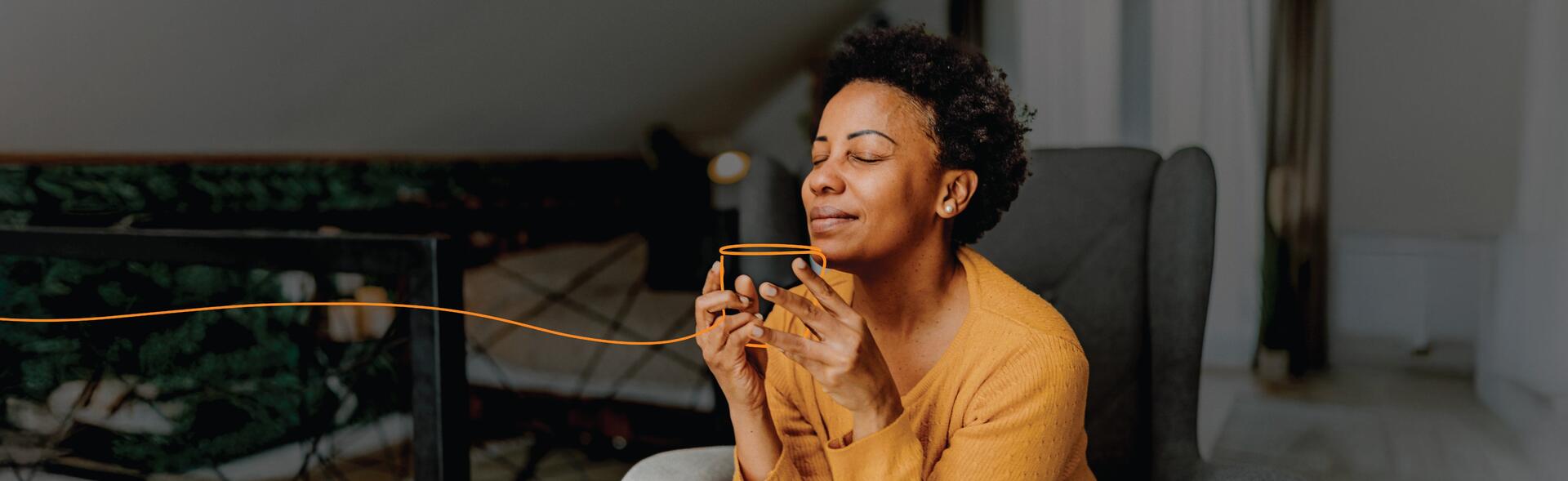 A woman taking a deep breath of her coffee while sitting in her bedroom.