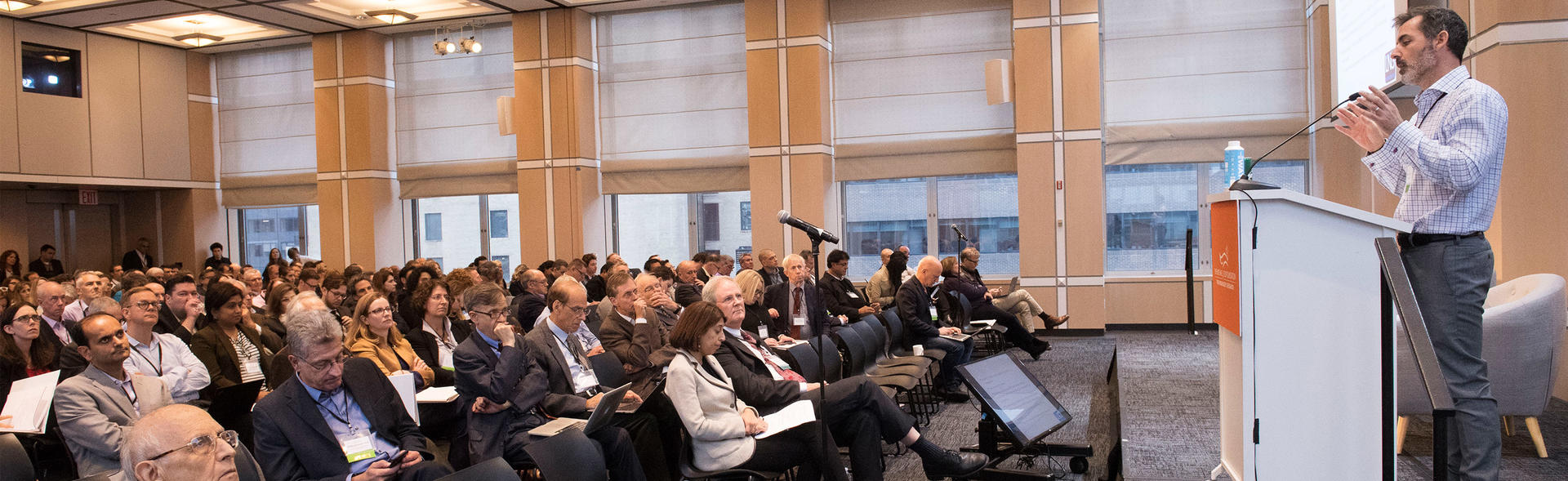 Scientist talking at a podium to group at a conference.