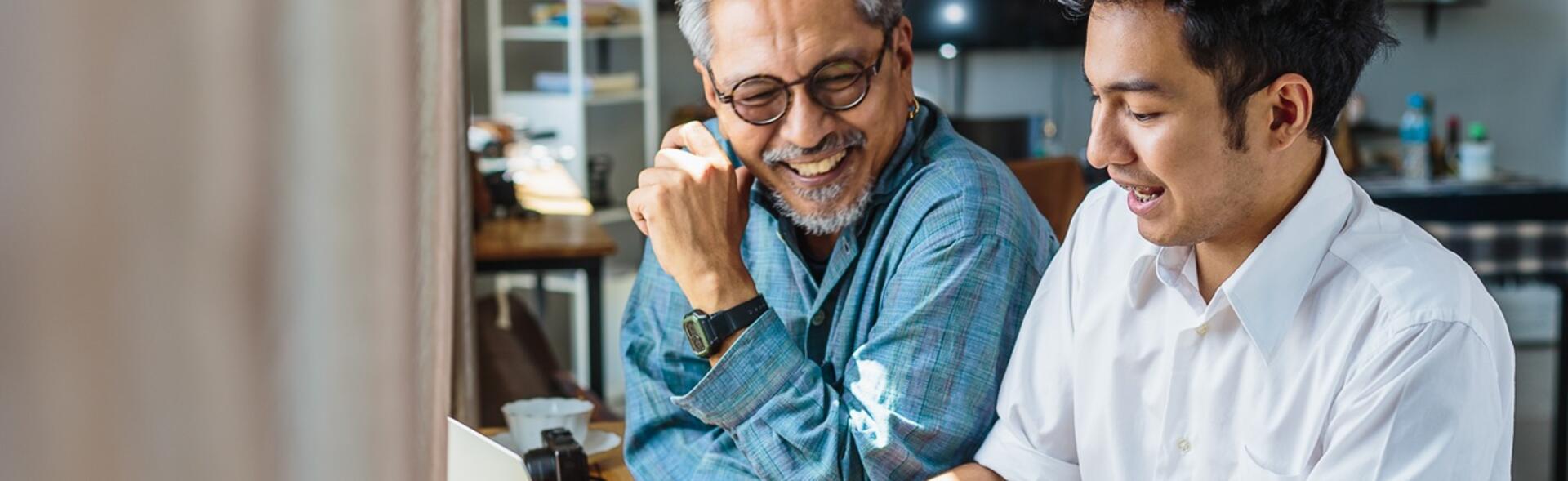 A father and son sitting at a desk looking a computer and smiling