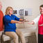Male care partner alongside female patient undergoing Parkinson's test with her female physician.