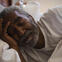 African American older man is asleep in bed. He wears a watch and is nestling his head with the other hand.