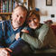 Male and female couple sitting on a couch smiling for the camera.