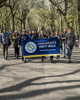 A crowd of people walk through a park for Parkinson's Unity Walk