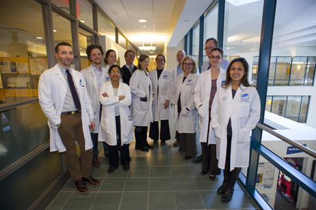 Group of 12 researchers in white coats posing for a picture in a lab.